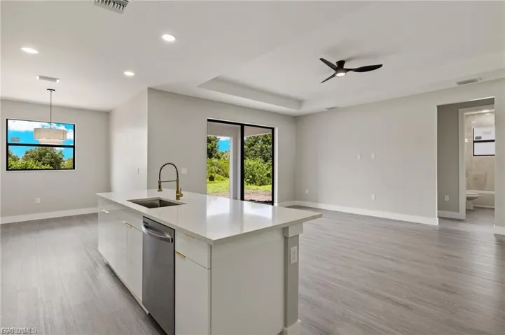 Kitchen featuring stainless steel dishwasher, light wood finished floors, a kitchen island with sink, light stone countertops, and white cabinets