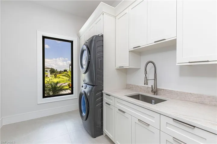 Laundry area featuring stacked appliances, ample white cabinetry, a utility sink with a high-arc faucet, and light-toned countertops