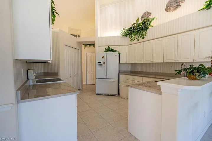 Kitchen with white fridge with ice dispenser, stove, light stone countertops, light tile patterned floors, and a towering ceiling