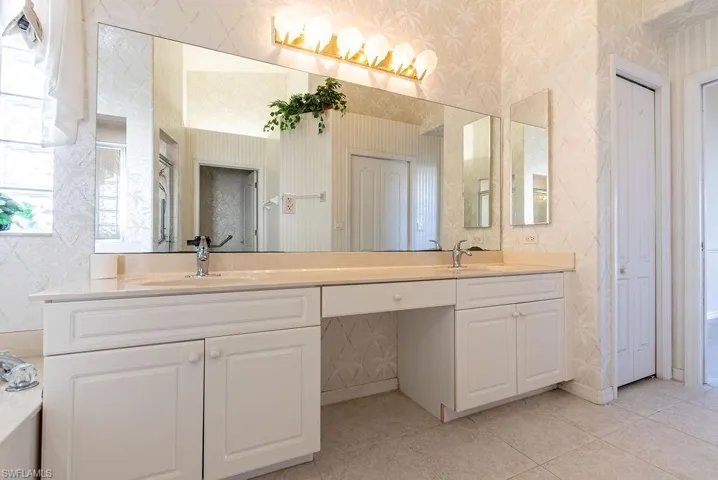 Bathroom with wallpapered walls, a closet, double vanity, light tile patterned floors, and a tub to relax in