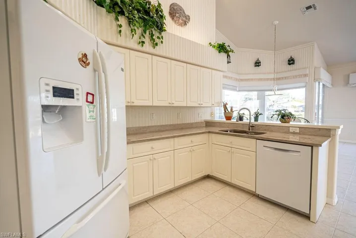 Kitchen with white appliances, a peninsula, light tile patterned flooring, hanging light fixtures, and a high ceiling