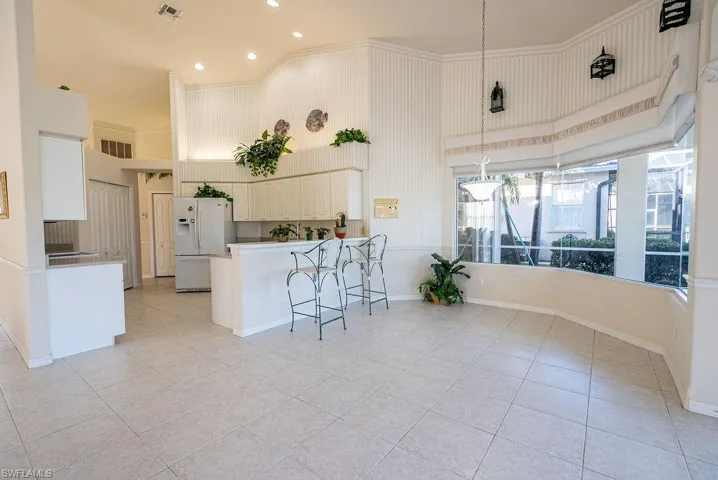 Kitchen with a breakfast bar area, white refrigerator with ice dispenser, hanging light fixtures, a towering ceiling, and a peninsula
