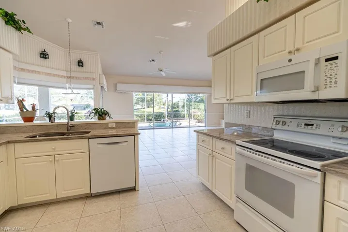 Kitchen with white appliances, a ceiling fan, light tile patterned floors, and light stone countertops