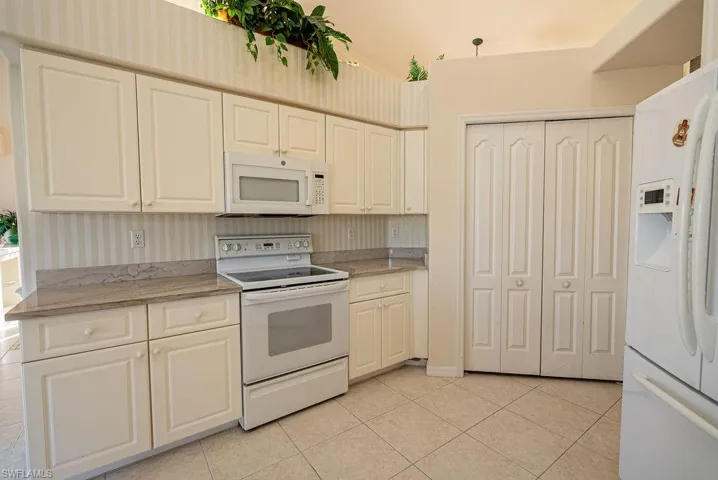 Kitchen featuring white appliances, light stone counters, light tile patterned flooring, and wallpapered walls