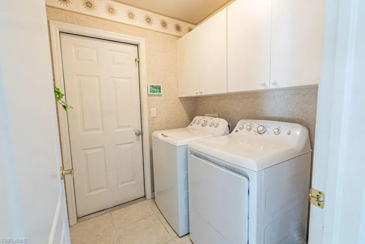 Washroom featuring wallpapered walls, cabinet space, washing machine and dryer, and light tile patterned floors