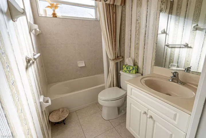 Full bathroom with vanity, shower / bathtub combination with curtain, wallpapered walls, and light tile patterned flooring