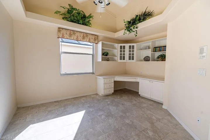 Unfurnished office featuring built in study area, a tray ceiling, and ceiling fan