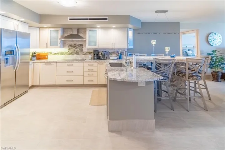 Kitchen featuring a breakfast bar, stainless steel refrigerator with ice dispenser, a peninsula, white cabinetry, and decorative backsplash