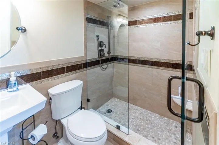 Bathroom featuring a shower stall, tile walls, and a wainscoted wall