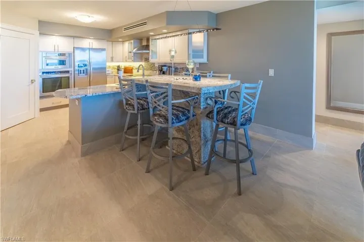 Kitchen featuring a peninsula, a kitchen bar, light stone counters, stainless steel refrigerator with ice dispenser, and white cabinetry