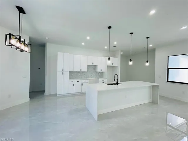 Kitchen with decorative light fixtures, white cabinets, an island with sink, and sink