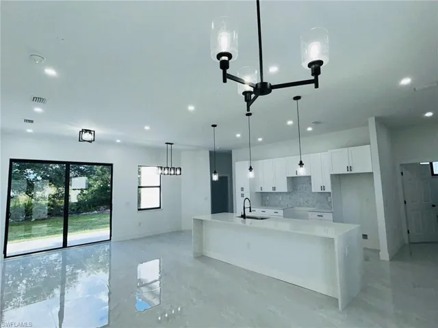 Kitchen with decorative light fixtures, a center island with sink, backsplash, sink, and white cabinets
