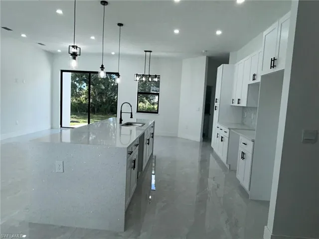 Kitchen featuring hanging light fixtures, light stone counters, sink, decorative backsplash, and a kitchen island with sink