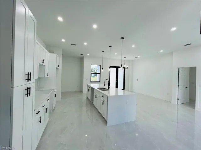 Kitchen featuring pendant lighting, sink, white cabinets, and a kitchen island with sink