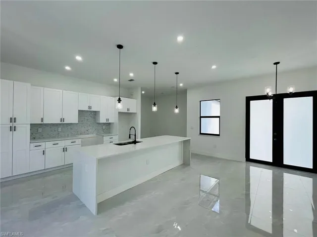 Kitchen with white cabinetry, an island with sink, sink, and decorative backsplash