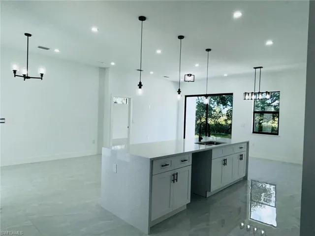 Kitchen with pendant lighting, sink, a center island with sink, and white cabinets
