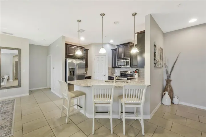 Kitchen featuring appliances with stainless steel finishes, tasteful backsplash, hanging light fixtures, light stone countertops, and dark brown cabinets
