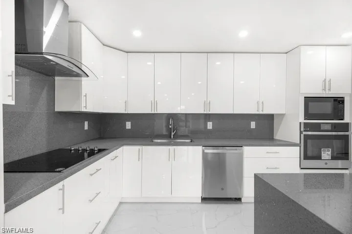 Kitchen with wall chimney range hood, black appliances, tasteful backsplash, dark stone counters, and white cabinets