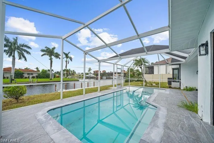 Swimming pool with screened enclosure, a sun shelf, a water view, and a patio area