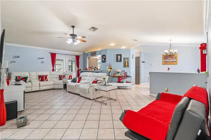Living room with crown molding, light tile patterned floors, a ceiling fan, and suspended lighting