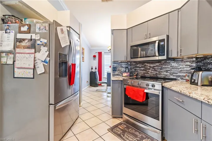 Kitchen with gray cabinetry, stainless steel appliances, ornamental molding, light stone countertops, and light tile patterned floors