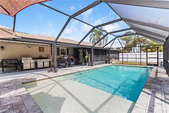 View of swimming pool featuring a lanai, exterior kitchen, a sunroom, and patio surround