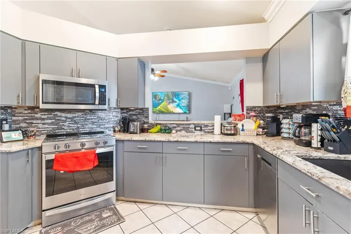 Two tone kitchen featuring stainless steel appliances, light stone counters, tasteful backsplash, crown molding, and light tile patterned flooring