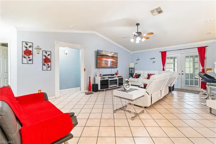 Living room featuring ornamental molding, lofted ceiling, a ceiling fan, french doors, and light tile patterned flooring