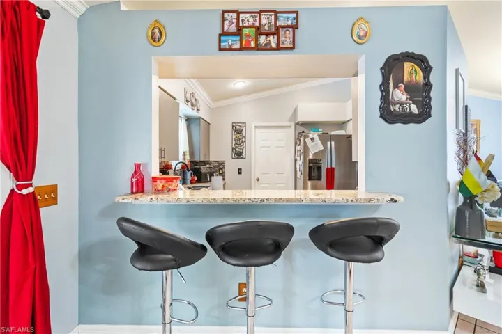 Kitchen featuring crown molding, stainless steel refrigerator with ice dispenser, a kitchen bar, white cabinetry, and light stone counters