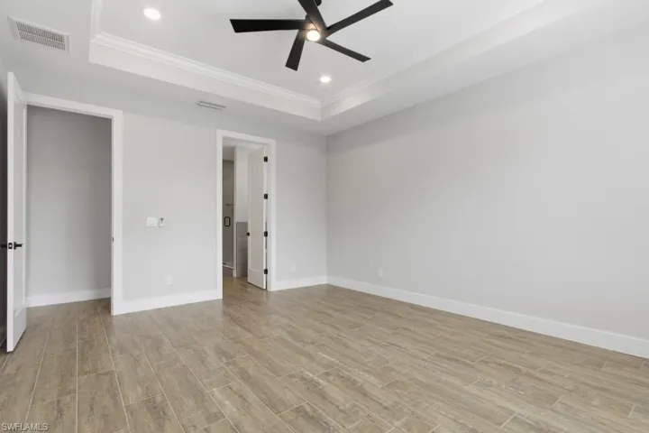 Unfurnished bedroom featuring a tray ceiling, wood tiled floors, ceiling fan, ornamental molding, and recessed lighting