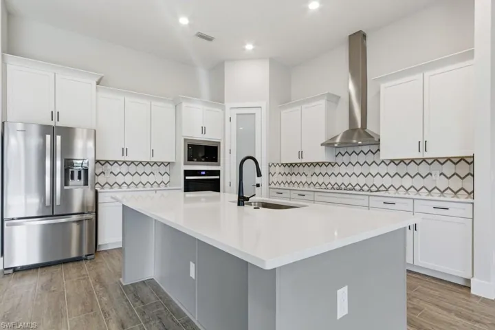 Kitchen with black appliances, white cabinets, wall chimney exhaust hood, an island with sink, and wood finish floors