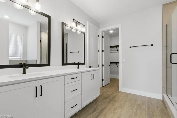 Full bathroom featuring double vanity, wood tiled floors, a walk in closet, and a stall shower
