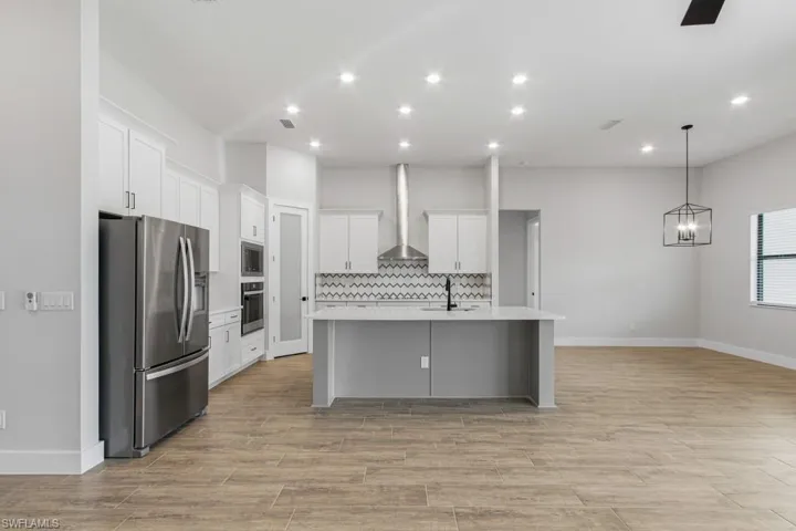 Kitchen featuring stainless steel appliances, white cabinets, an island with sink, hanging light fixtures, and tasteful backsplash