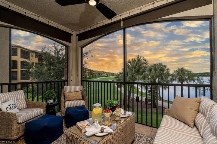 Screened balcony featuring a ceiling fan, a golf course, a body of water, and palm trees