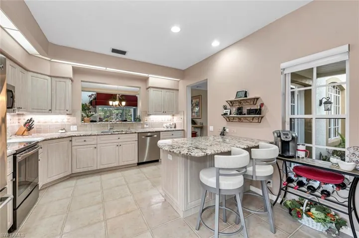 Kitchen with a breakfast bar, sink, decorative backsplash, light stone counters, and stainless steel appliances
