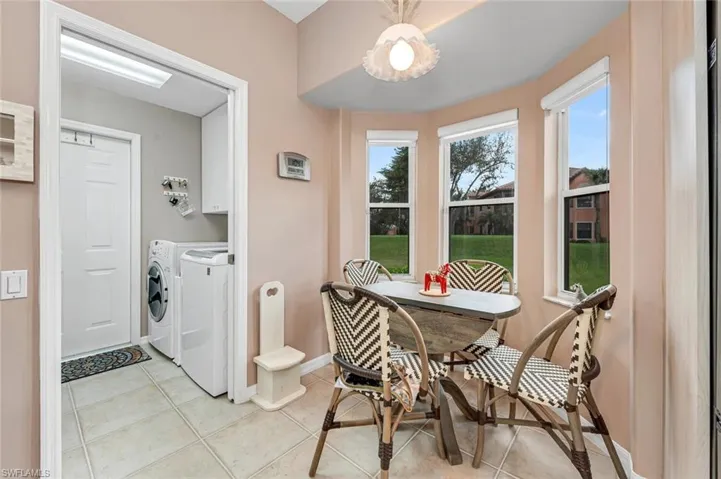 Clothes washing area with light tile patterned floors, washer and clothes dryer, and cabinets