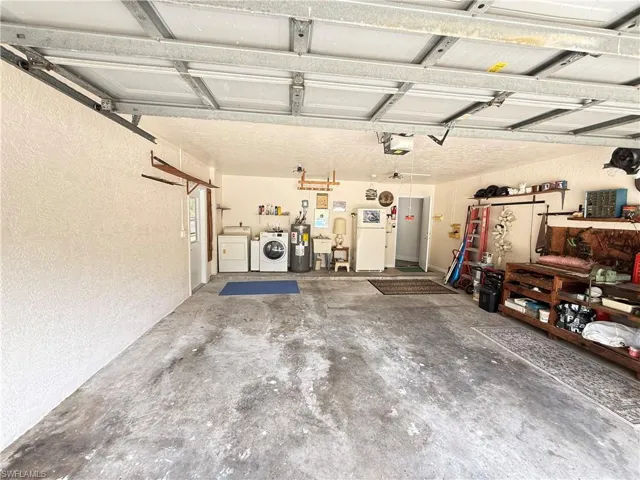 Garage with a textured wall, independent washer and dryer, freestanding refrigerator, water heater, and a garage door opener
