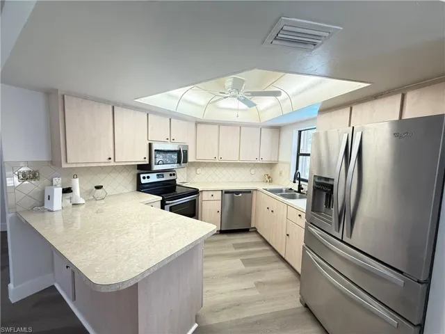 Kitchen featuring stainless steel appliances, light wood finish cabinets, light countertops, a peninsula, and light laminate flooring