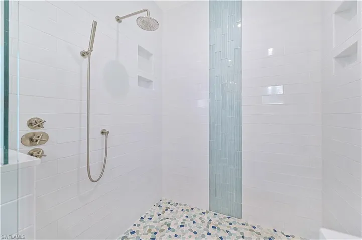 Shower enclosure featuring white subway tile walls, a vertical accent of blue glass tiles, a pebble-finish tiled floor, multiple recessed niches, and brushed nickel fixtures including a rain showerhead and handheld sprayer
