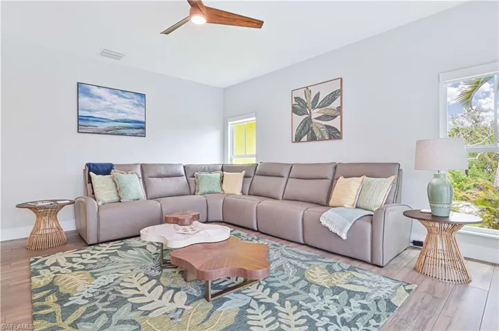 Spacious living area featuring wood-finish flooring, a ceiling fan with wood-finish blades, and multiple windows providing natural light