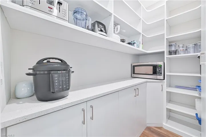 Walk-in pantry featuring extensive white shelving, white perimeter countertops, white cabinetry with silver-tone hardware, and wood-finish flooring