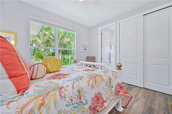 Bright room featuring a large window, wood-finish flooring, white sliding closet doors, and a ceiling fan