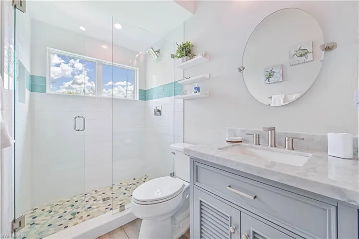 Contemporary bathroom featuring a glass-enclosed shower with mosaic tile flooring, a horizontal accent tile band, and a window for natural light
