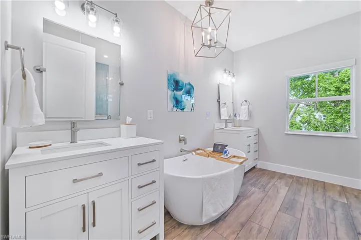 Spacious bathroom featuring wood-finish flooring, a standalone soaking tub, and a dual vanity with white cabinetry and brushed nickel hardware