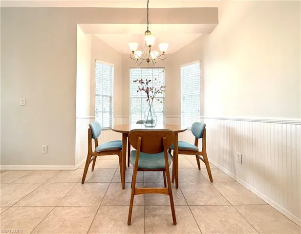 Dining area with light tile patterned floors, a wainscoted wall, and a chandelier