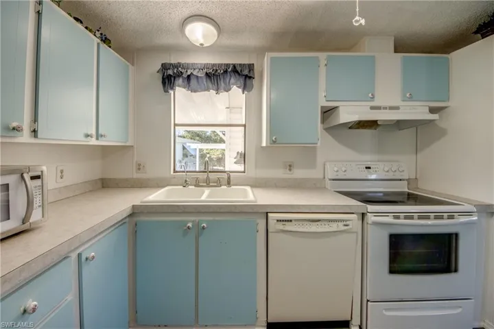 Kitchen featuring blue cabinetry, white appliances, light countertops, under cabinet range hood, and a textured ceiling