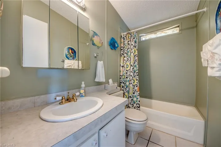 Bathroom featuring a textured ceiling, shower / tub combo, light tile patterned floors, and vanity