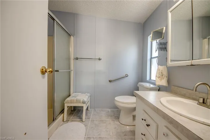 Bathroom featuring a shower stall, vanity, a textured ceiling, and light tile patterned floors