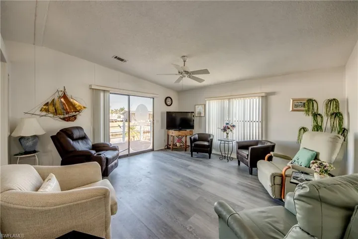 Living room with lofted ceiling, a textured ceiling, wood finished floors, and ceiling fan