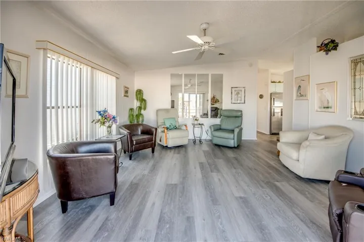 Living room with vaulted ceiling, a ceiling fan, a textured ceiling, and wood finished floors